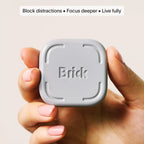 Hand holding the light gray Brick physical device displaying the text 'Block distractions. Focus deeper. Live fully.'