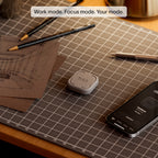 Brick device and smartphone on a cutting mat showing custom modes like Work Mode and Focus Mode.