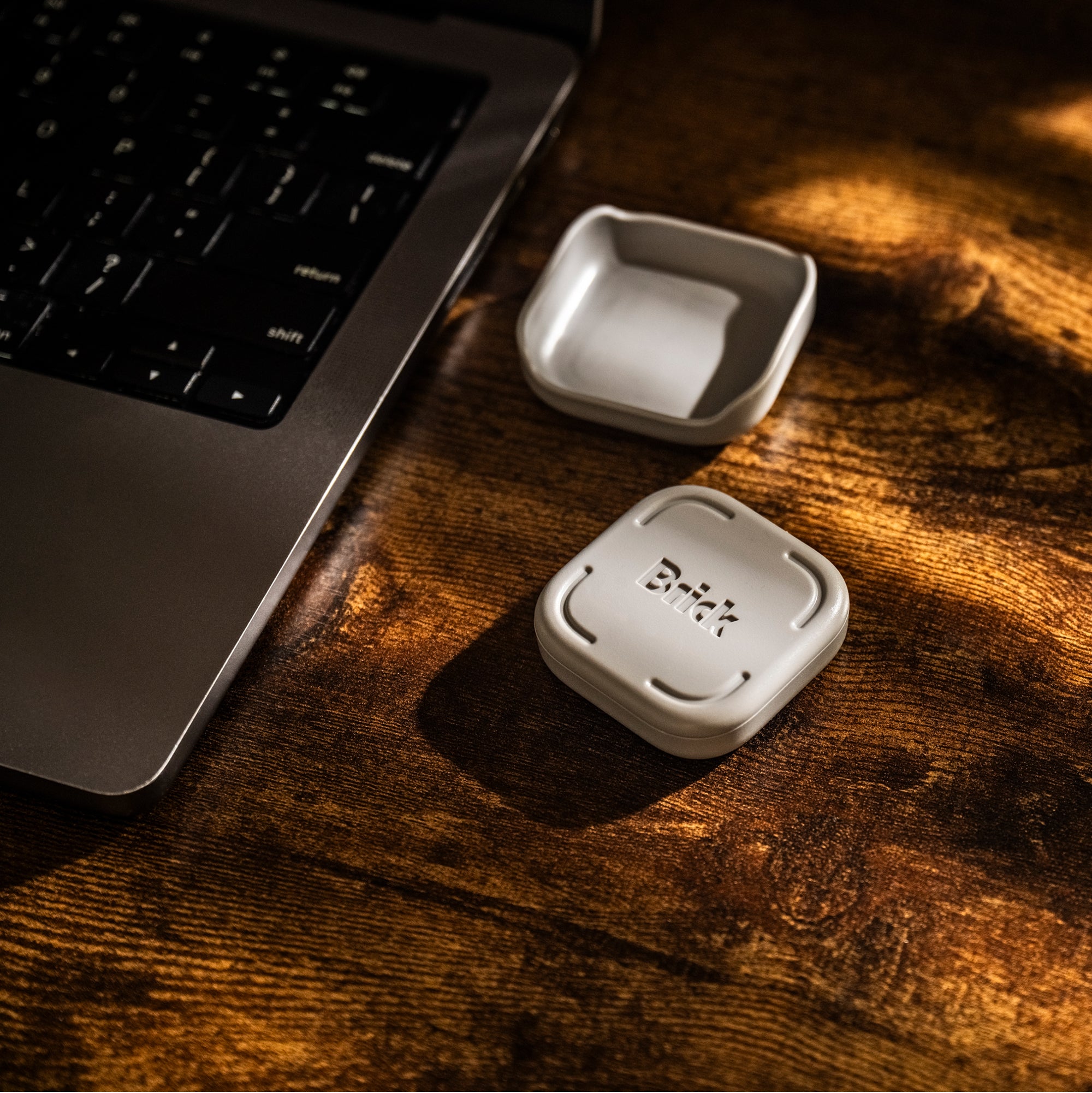 Brick device resting in its wall mount next to a laptop on a dark wooden desk.