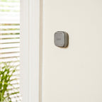 Brick device docked in a gray wall mount attached to a plain off-white wall near a window.