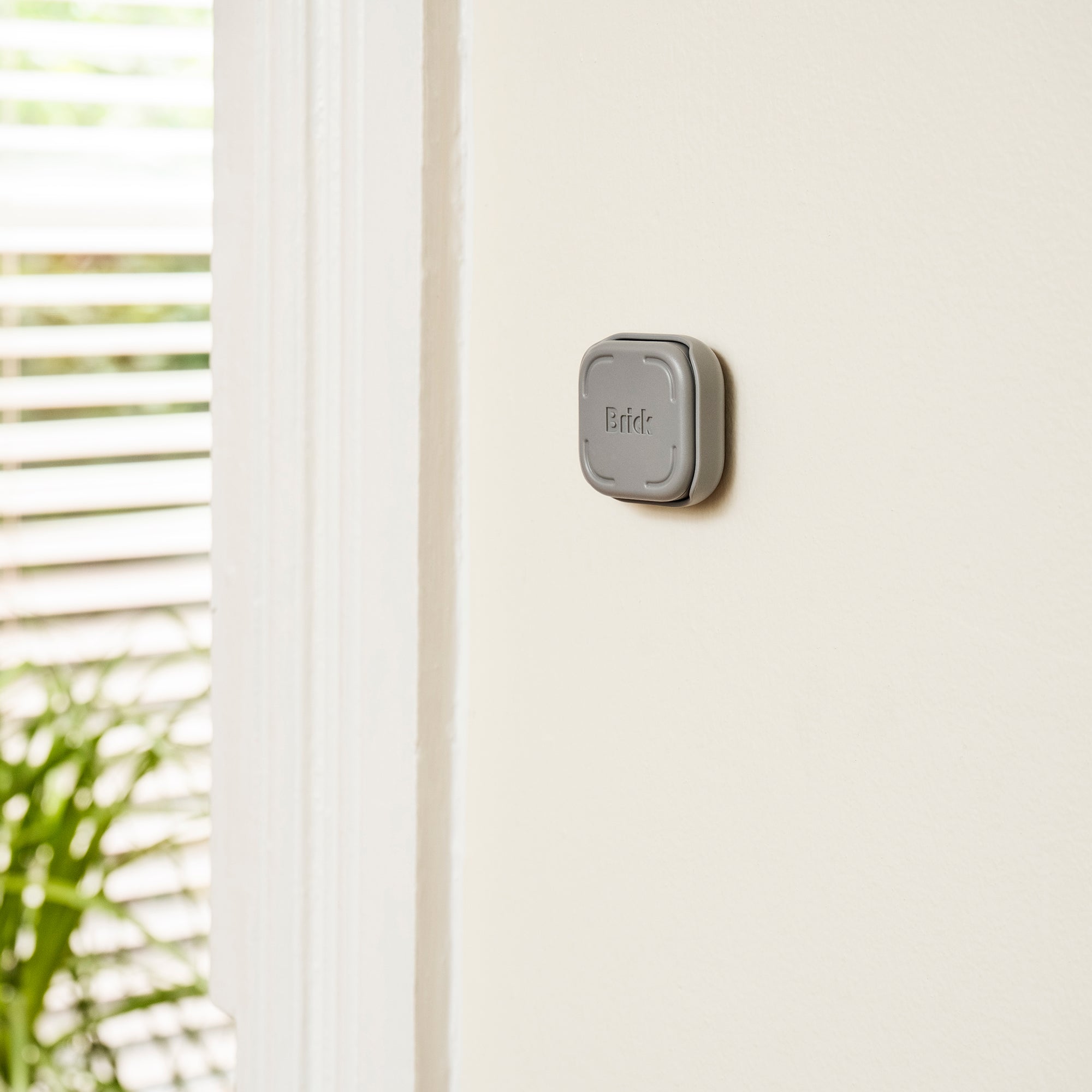 Brick device docked in a gray wall mount attached to a plain off-white wall near a window.