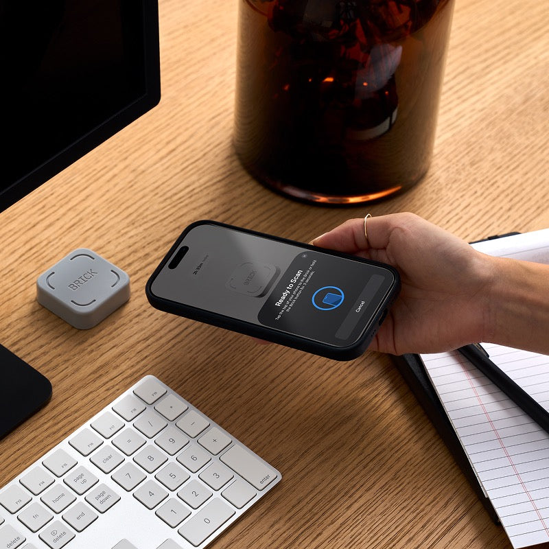 Person holding a smartphone over a desk with a keyboard, monitor, and bottle.