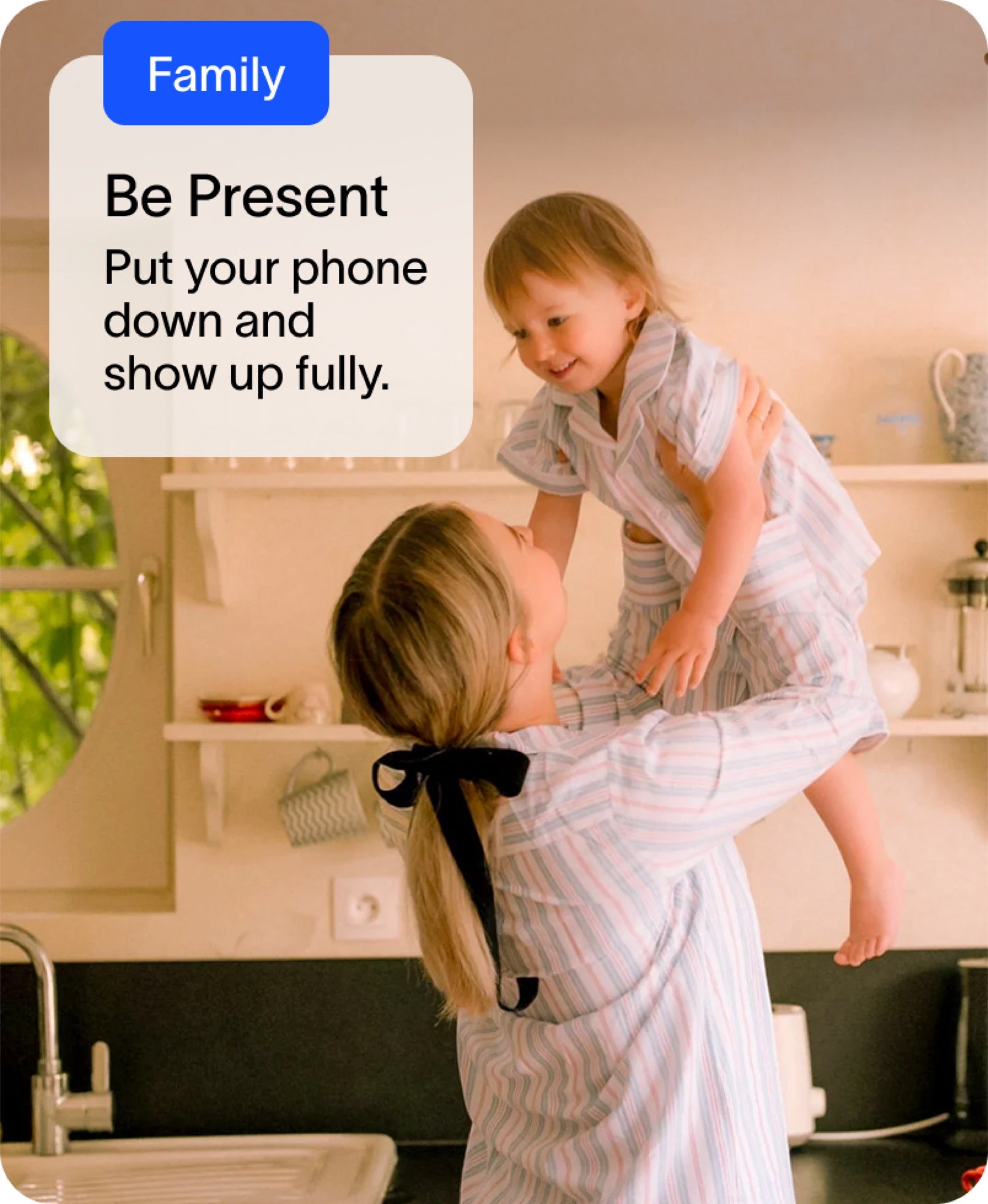 Woman lifting a child in a kitchen with a text bubble about being present and putting down the phone to shop up fully
