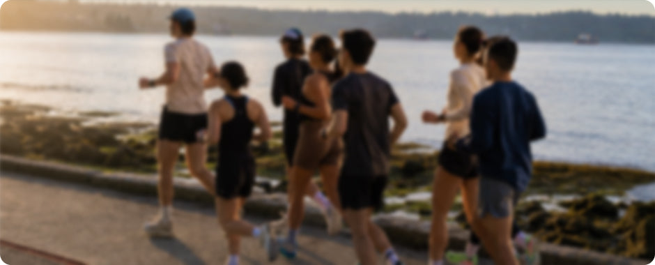 A group of people jogging along a waterfront path during late afternoon, with water and distant land visible in the background.