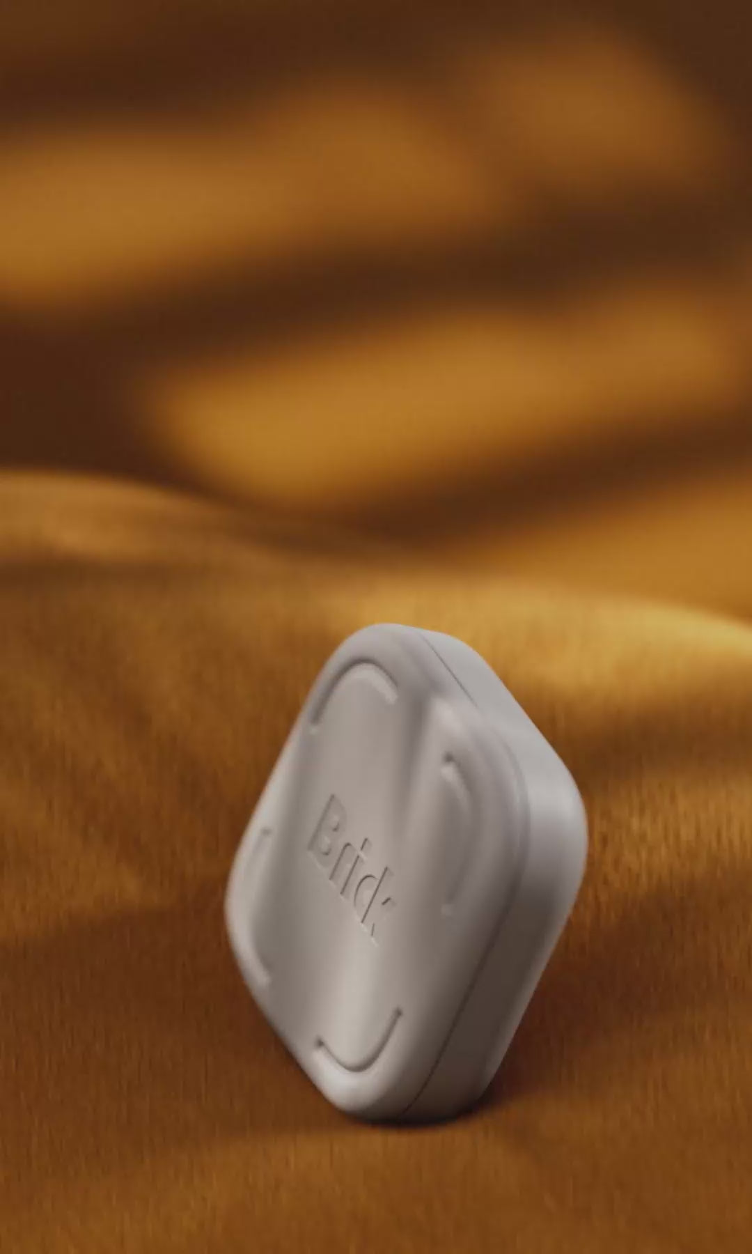 Close-up looping video of the light gray, square Brick device standing upright across different settings, including cozy fabric, a kitchen counter, a blue grid work desk, green grass, and a wooden table.